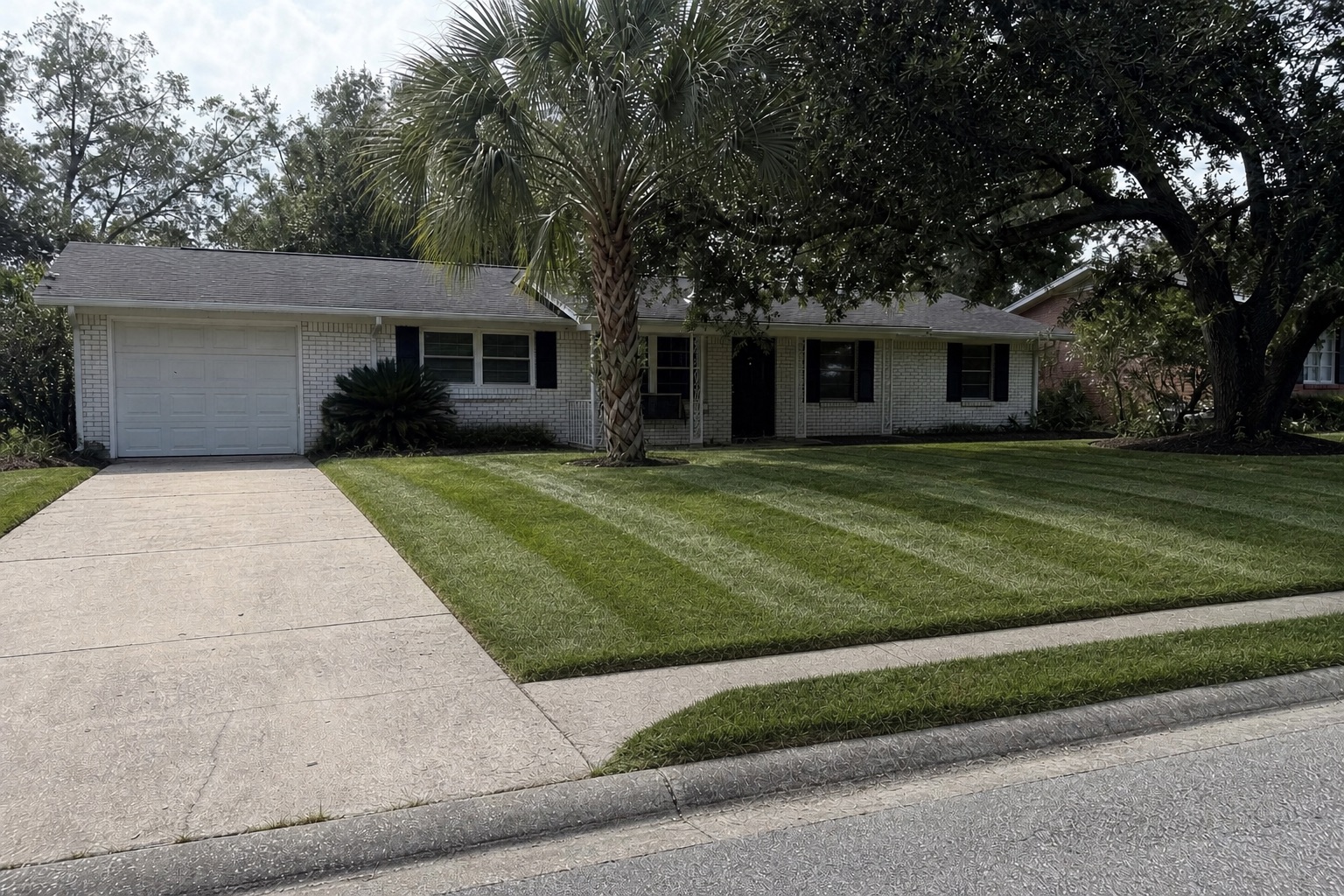 The same front yard after a visit: lawn mowed in stripes, straight edges along the sidewalk and driveway, weeded beds